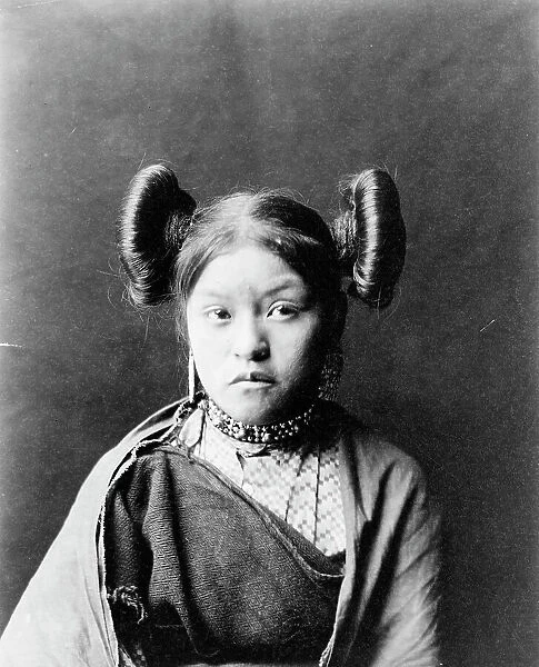 Gobuguoy, Walpi girl, half-length portrait, facing front, hair tied in swirls on sides of... c1900. Creator: Edward Sheriff Curtis