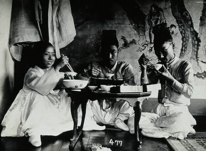 Framed Print : A group of people eating a meal, seated behind a small table, in front of a painted screen, c1900. Creator: Unknown Framed Print : A group of people eating a meal, seated behind a small table, in front of a painted screen, c1900. Creator: Unknown