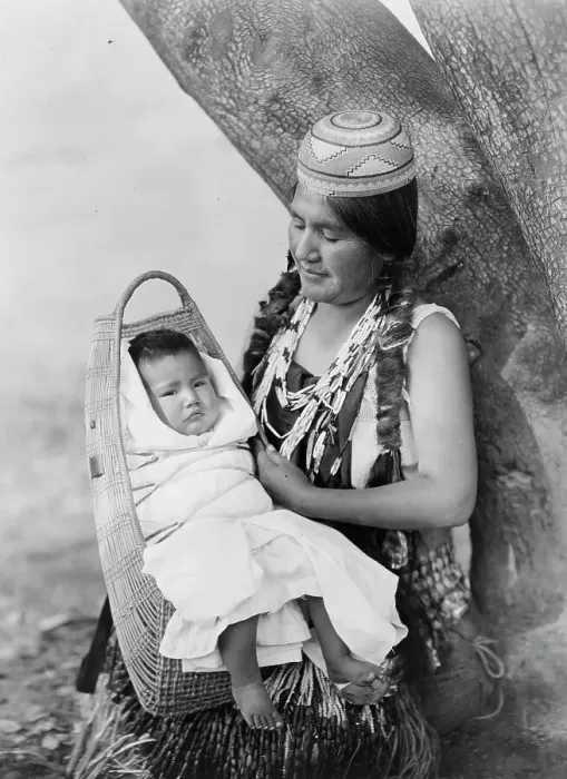 Framed Print : Hupa mother, three-quarter length portrait, seated, facing left, holding baby, c1923. Creator: Edward Sheriff Curtis