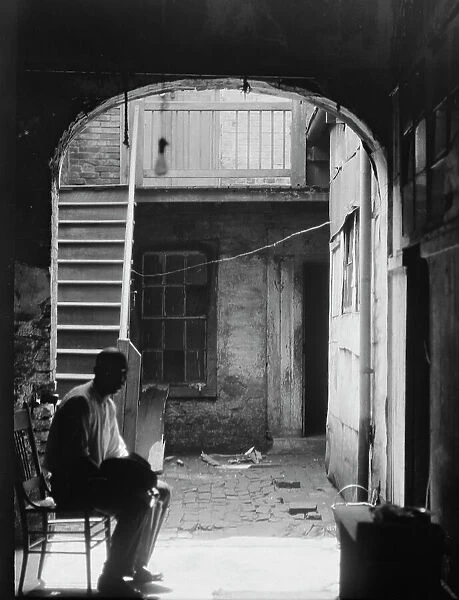 Man seated in archway leading to a courtyard, New Orleans, between 1920 and 1926. Creator: Arnold Genthe