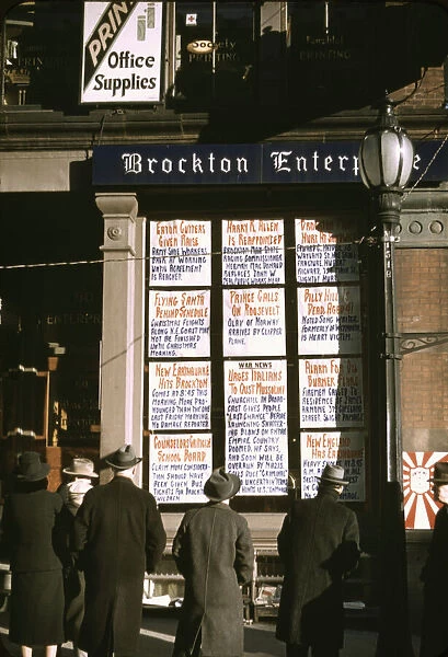 Men and a woman reading headlines posted in street-corner window of Brockton... Mass. 1940. Creator: Jack Delano