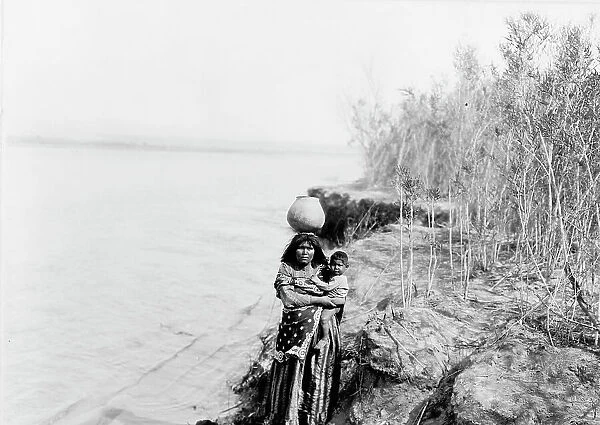 Mohave woman carrying water on her head and holding child, c1903. Creator: Edward Sheriff Curtis