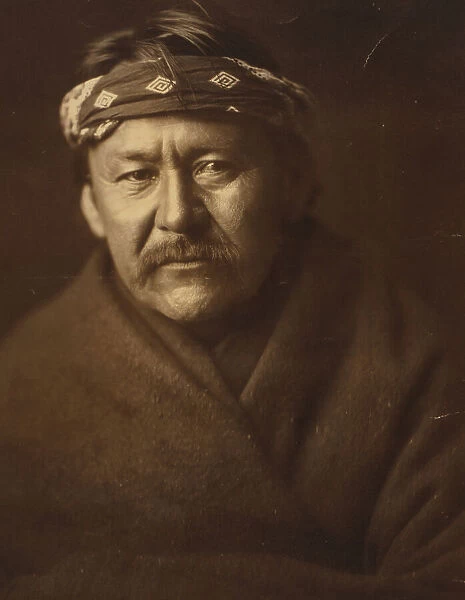 A Navajo man, head-and-shoulders portrait, wearing blanket and headband, facing front, c1904. Creator: Edward Sheriff Curtis