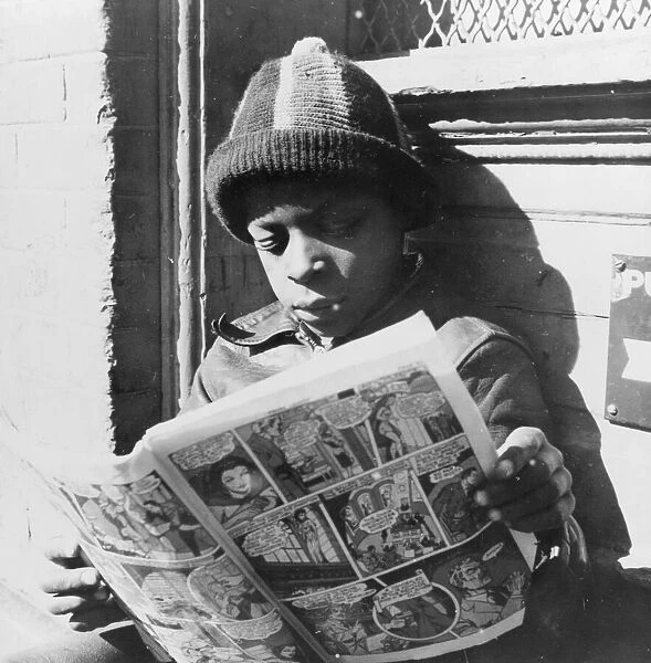 Negro youth reading a funny paper on a door step in the Southwest section, Washington, D. C. 1942. Creator: Gordon Parks
