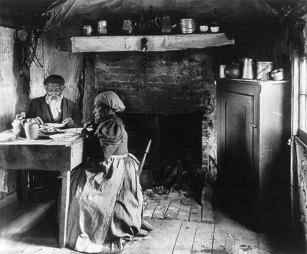Old African American couple eating at the table by fireplace, rural Virginia, 1899 or 1900. Creator: Frances Benjamin Johnston