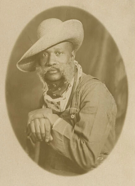 Photographic postcard portrait of a man wearing a hat and overalls, early 20th century