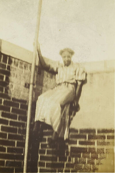 Photographic print of a woman on a brick wall, early 20th century. Creator: Unknown