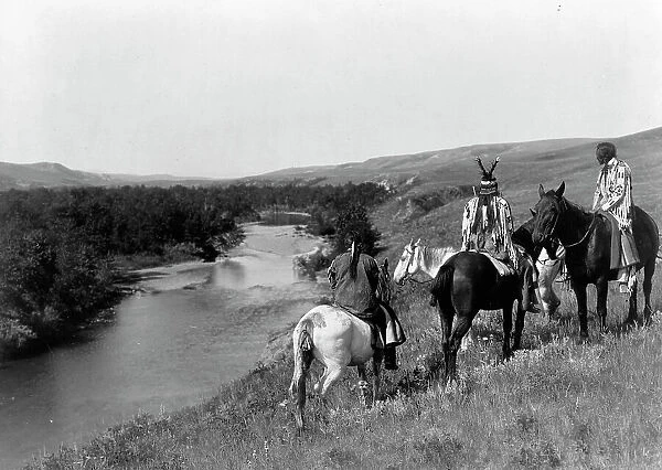 Three Piegan Indians and four horses on hill above river, c1910. Creator: Edward Sheriff Curtis