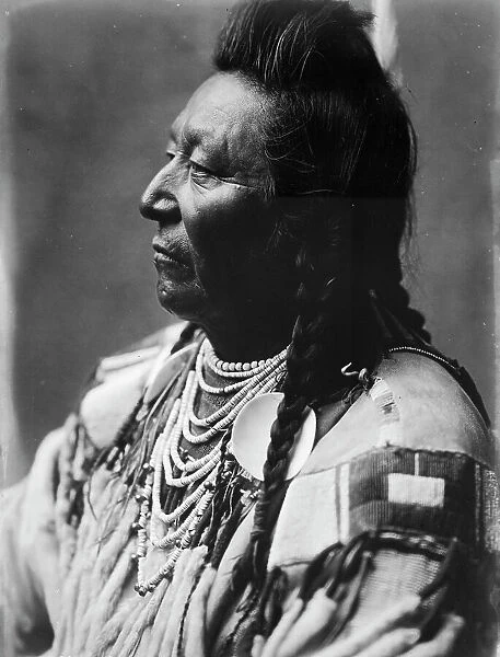 Plenty Coups, Crow Indian, head-and-shoulders portrait, facing left, pompadour, temple... c1908. Creator: Edward Sheriff Curtis