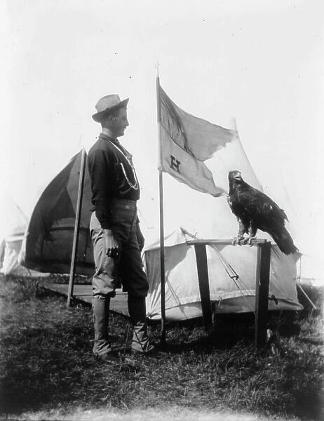 Soldier and eagle mascot beside 'H' Troop flag, 1898. Creator: Frances Benjamin Johnston. Soldier and eagle mascot beside 'H' Troop flag, 1898. Creator: Frances Benjamin Johnston