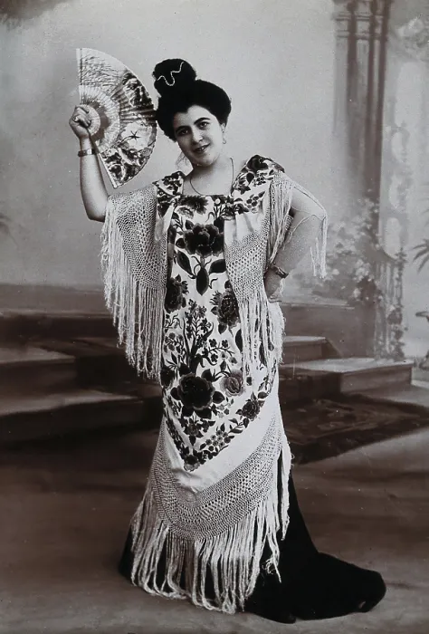 Framed Print : A standing woman, holding aloft a fan, wearing a fringed shawl, in front of a painted... c1900. Creator: Unknown Framed Print : A standing woman, holding aloft a fan, wearing a fringed shawl, in front of a painted... c1900. Creator: Unknown