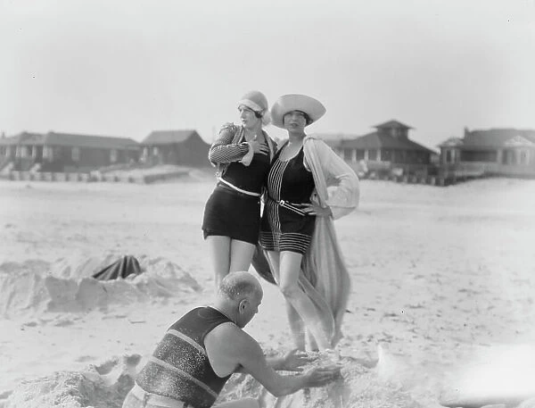 Unidentified man building sand castle and two women, Long Beach, New York, between 1911 and 1942. Creator: Arnold Genthe