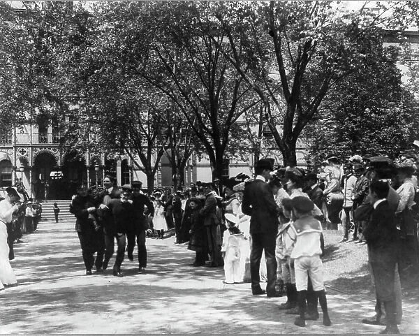 U.S. Naval Academy, Annapolis: 4 midshipmen carrying a man; crowd of guests along sidewalk, (1902?). Creator: Frances Benjamin Johnston