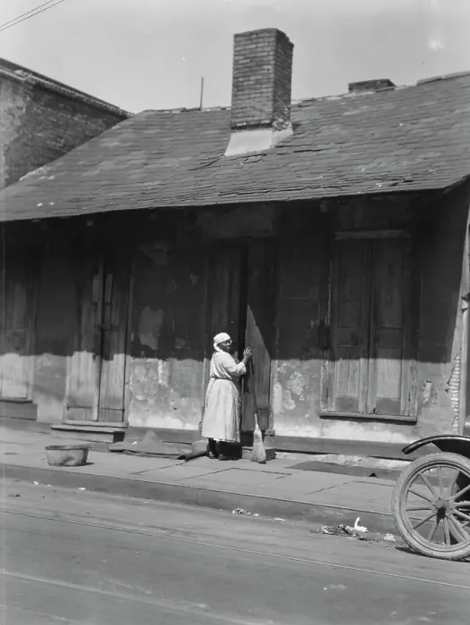 Framed Print : View from across street of a woman with a broom standing in a doorway, New Orleans, c1920-c1926. Creator: Arnold Genthe Framed Print : View from across street of a woman with a broom standing in a doorway, New Orleans, c1920-c1926. Creator: Arnold Genthe