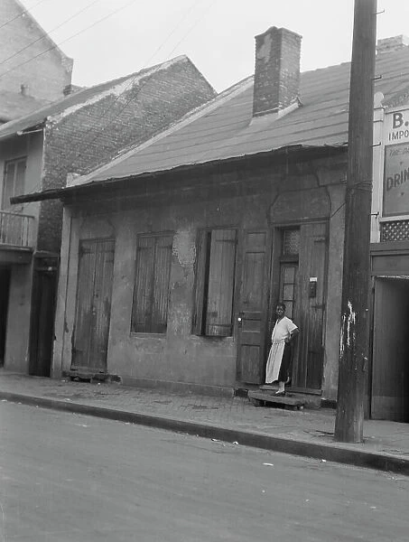 View from across street of a woman standing by a doorway in the French Quarter, New... c1920-c1926. Creator: Arnold Genthe