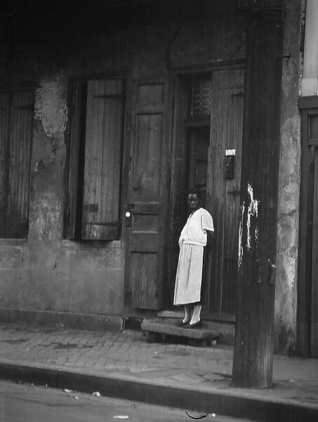 View from across street of a woman standing in a doorway in the French Quarter, New... c1920-c1926. Creator: Arnold Genthe