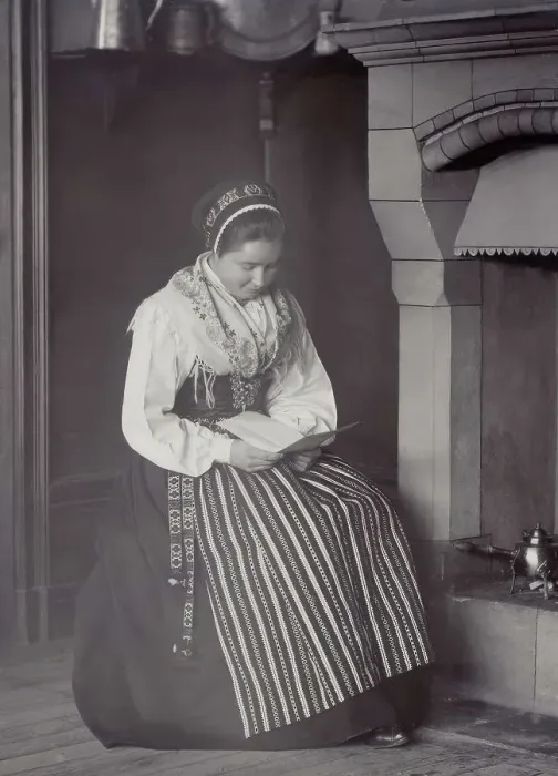 Framed Print : A woman sits in front of a fireplace and reads dressed in a Dalarna costume, 1886-1920. Creator: Helene Edlund Framed Print : A woman sits in front of a fireplace and reads dressed in a Dalarna costume, 1886-1920. Creator: Helene Edlund