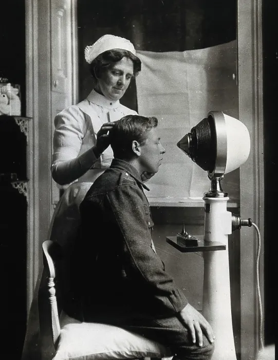 Framed Print : A young uniformed man sitting with a pillow on his chair, facing a machine... c1910s. Creator: Unknown Framed Print : A young uniformed man sitting with a pillow on his chair, facing a machine... c1910s. Creator: Unknown