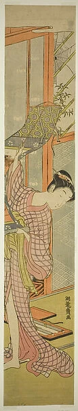 Young Woman Hanging a Painting, c. 1771. Creator: Isoda Koryusai