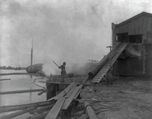 Lumber Yard Prints: African American guiding log from water onto saw mill ramp