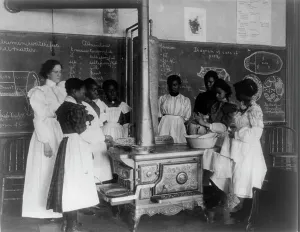 African American schoolgirls with teacher, learning to cook on a wood stove in classroom, (1899?). Creator: Frances Benjamin Johnston