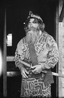 Aino Prints: Ainu chief wearing a headdress and holding a sword standing in a doorway