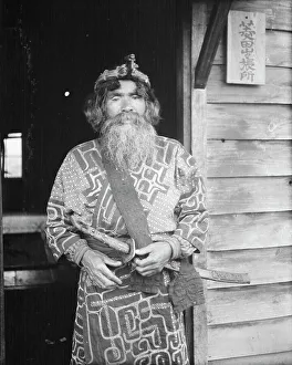 Aino Prints: Ainu chief wearing a headdress and holding a sword standing in a doorway