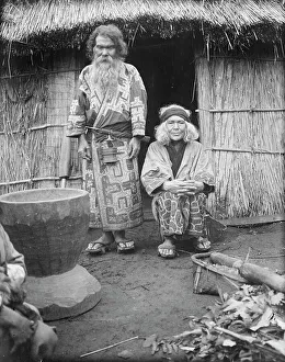 Ainu man and seated woman at the entrance of a hut, 1908. Creator: Arnold Genthe