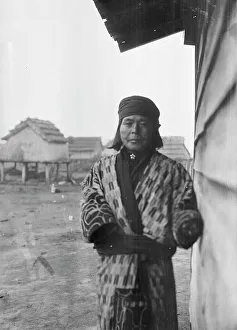 Stilts Prints: Ainu standing outside by the wall of a wooden hut, 1908. Creator: Arnold Genthe