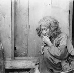 Ainu woman seated by the door of a wooden hut, 1908. Creator: Arnold Genthe