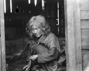 Ainu woman seated in the doorway of a wooden hut, 1908. Creator: Arnold Genthe
