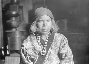 Aino Prints: Ainu woman wearing a headscarf, earrings, and a necklace, 1908. Creator: Arnold Genthe