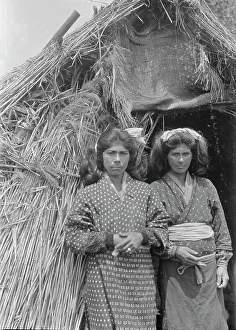 Two Ainu women standing at the entrance of a hut, 1908. Creator: Arnold Genthe