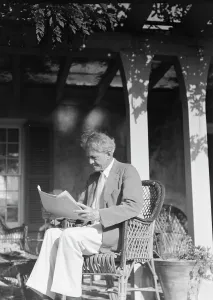 Arnold Genthe seated outdoors in a wicker chair reading, between 1911 and 1942. Creator: Arnold Genthe