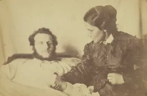 Sickbed Prints: A bearded man lying in bed, his hand held by his wife who is seated next to the bed