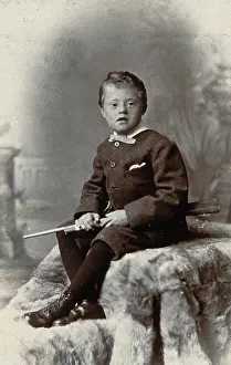 Mental Health Prints: A boy with Down's syndrome, holding a rifle and sitting on a fur carpet, c1900