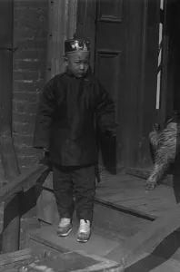 Boy standing on steps in front of a doorway, Chinatown, San Francisco, between 1896 and 1906. Creator: Arnold Genthe