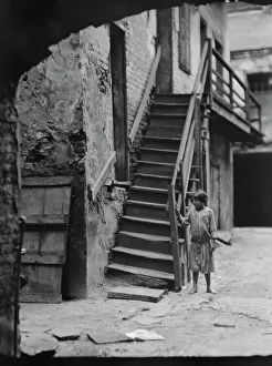 Child standing next to a stairway in a courtyard, New Orleans, between 1920 and 1926. Creator: Arnold Genthe