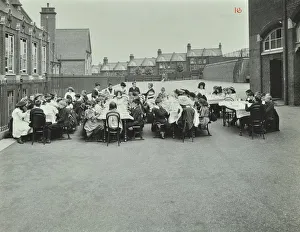Woolwich Prints: Children eating dinner at tables in the playground