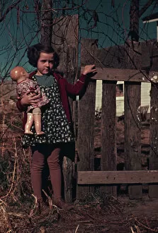 Girl with doll standing by fence, between 1941 and 1942. Creator: Unknown