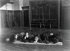 Gymnasium Prints: Five girls lying on mat in gymnasium in front of basketball scoreboard