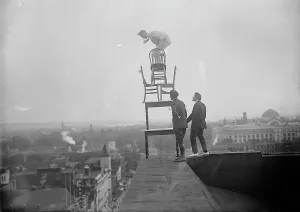 Publicity Stunt Prints: J. Reynolds, Performing Acrobatic And Balancing Acts On High Cornice Above 9th Street