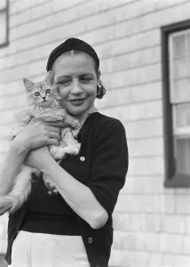 Headwrap Prints: Leonard, Mrs. with cat, standing outdoors, between 1926 and 1938. Creator: Arnold Genthe