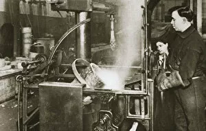 Lowering Gallery: Making money; lowering a pot of liquid metal into a machine, 20th century. Artist