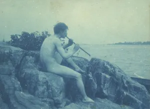 Man posed on rocks, nude, playing pipe (Pan), between 1885 and 1900. Creator: Frances Benjamin Johnston