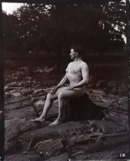 A man posing naked, seated on a rocky outcrop in a leafy landscape, c1900. Creator: Unknown