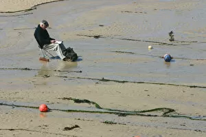 Cornish Gallery: Man sitting on the sand in St Ives harbour at low tide, Cornwall