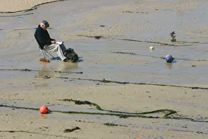 Cornish Gallery: Man sitting on the sand in St Ives harbour at low tide, Cornwall