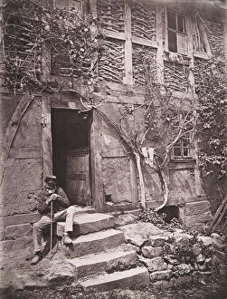 [Man Sitting on Steps of House with Socks Hanging on Nearby Vine to Dry], 1880s