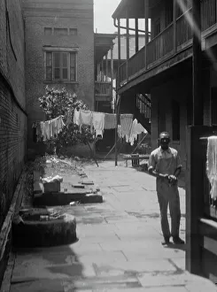 Clothes Line Prints: Man standing in a courtyard, New Orleans, between 1920 and 1926. Creator: Arnold Genthe